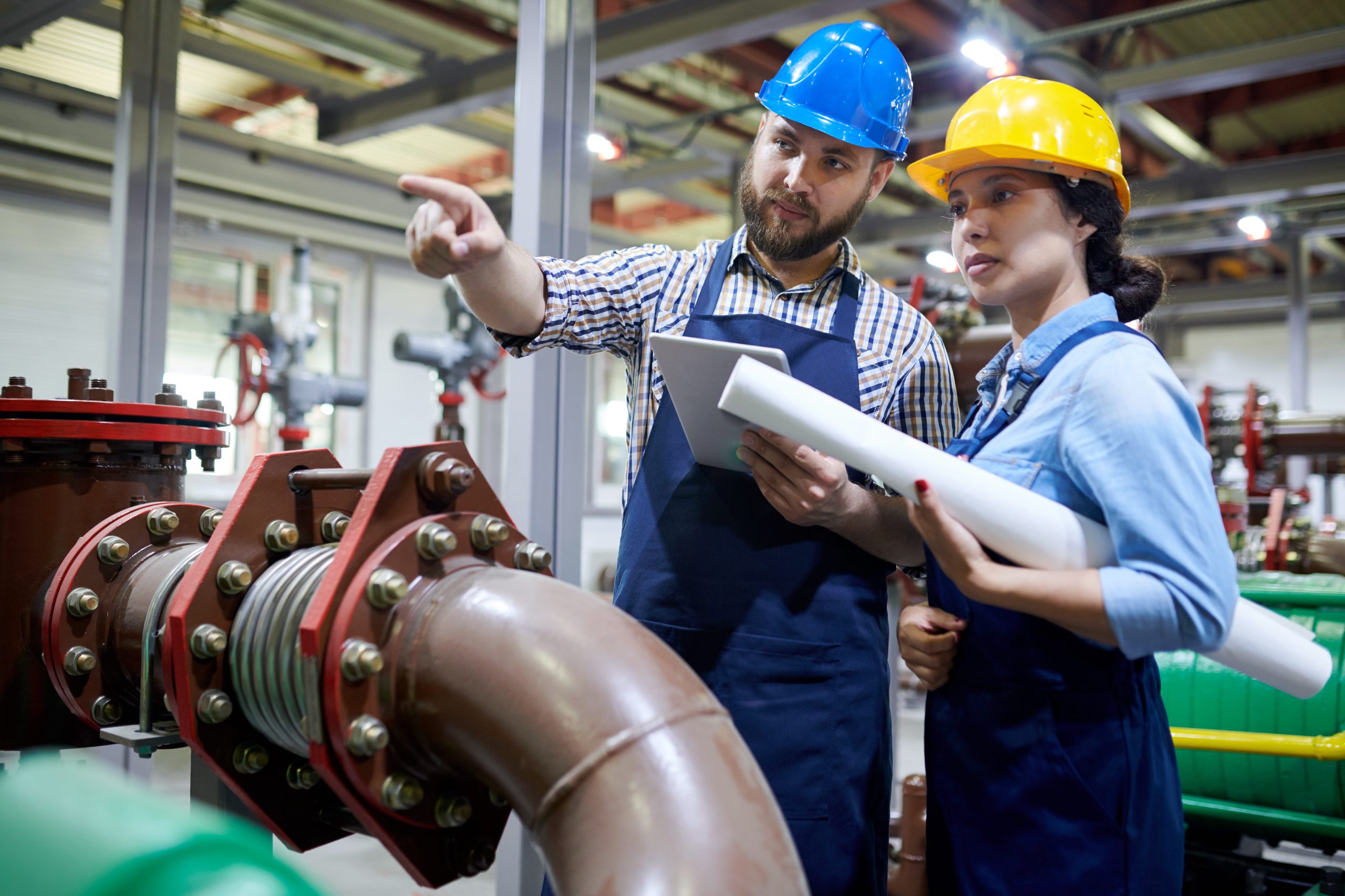 Portrait of two factory workers pointing away while working with piping and machines in modern workshop, copy space